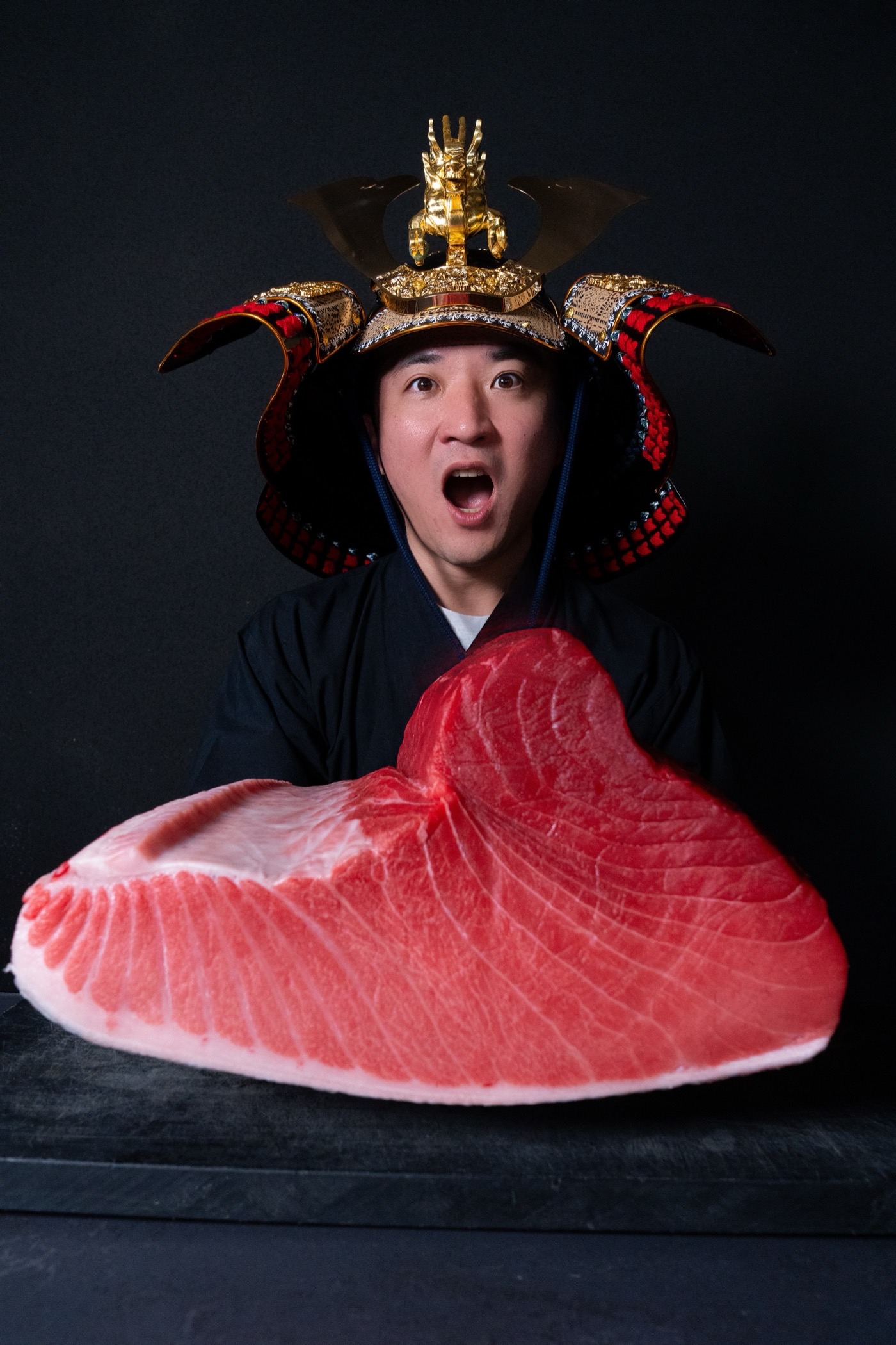Norikazu Takagi, founder of TUNASHOGUN, wearing a kabuto helmet behind a whole bluefin tuna loin