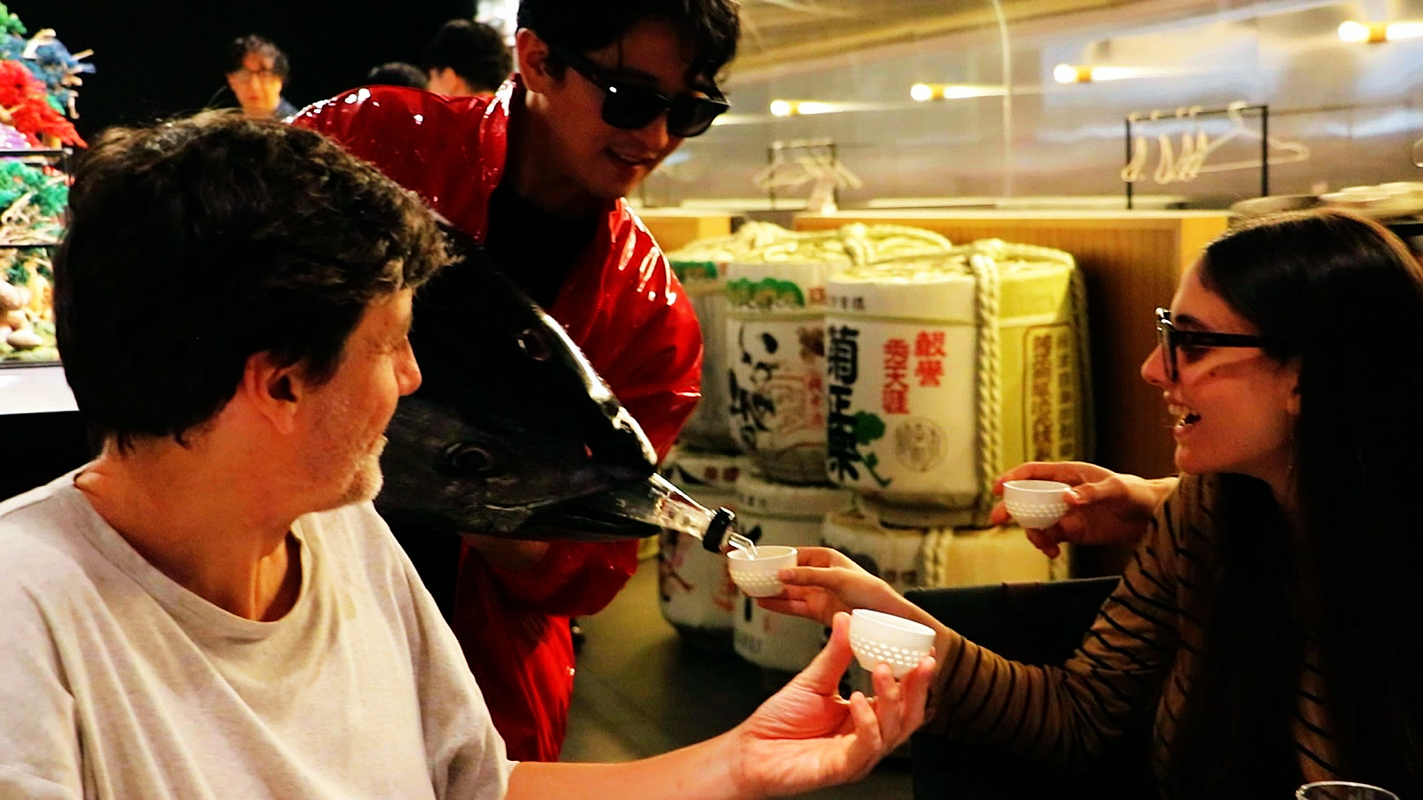 Guests hold out their cups as sake is poured from the tuna head