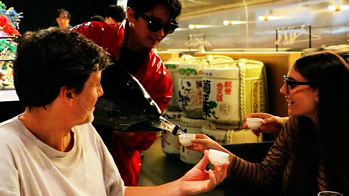 Guests hold out cups as sake is poured from the tuna head