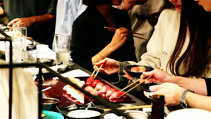 Guests reaching for tuna nigiri with chopsticks